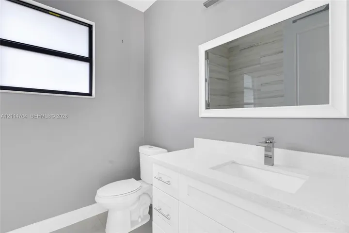 White vanity featuring a solid-surface countertop with an integrated rectangular sink and polished chrome faucet, paired with a white-framed wall mirror, and a ceramic toilet