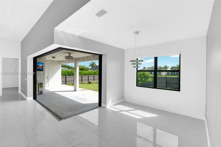 Large-format tile flooring, retractable glass wall system, multi-tiered pendant lighting, and covered patio area with concrete hardscaping