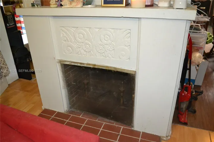 Fireplace surround featuring a decorative carved frieze, a mantle shelf, and a brick-lined firebox with a protective screen, accented by a tile hearth