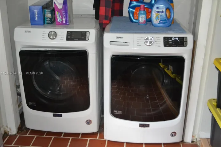 Laundry area featuring white front-load washer and dryer units with digital interfaces and ceramic tile flooring