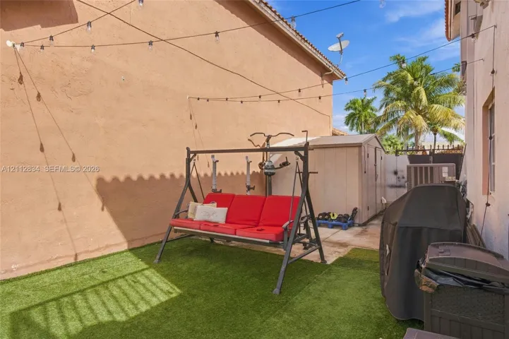 Side yard featuring artificial turf, string lighting, and a neutral-toned storage shed