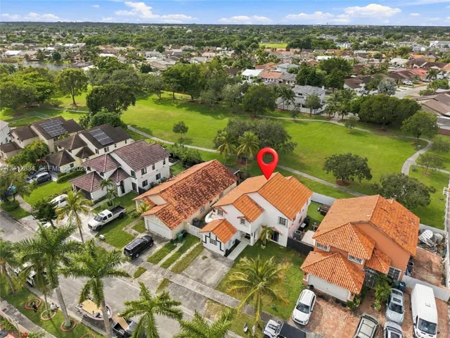 Two-story residence featuring a tile roof, concrete driveway, and established landscaping, situated on a lot bordering a large grass-covered common area