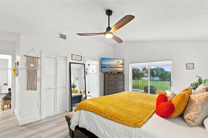 Vaulted ceiling featuring a three-blade matte black ceiling fan, louvered-style closet doors, and sliding glass doors providing outdoor access