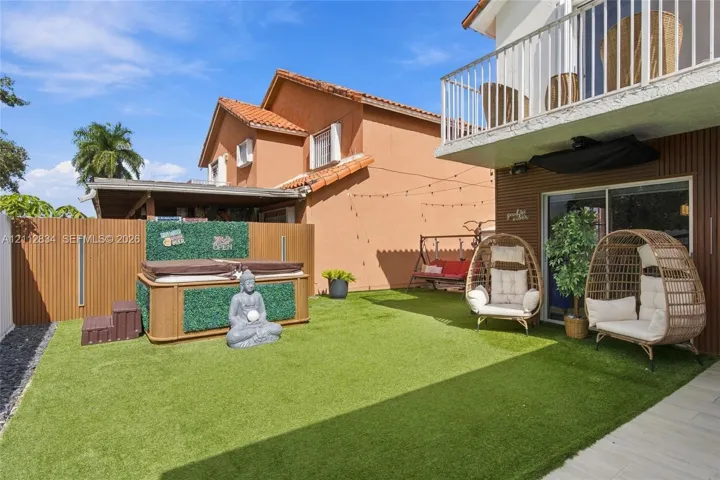 Fenced backyard featuring synthetic turf, wood-finish privacy fencing, and an upper-level balcony with white metal railings