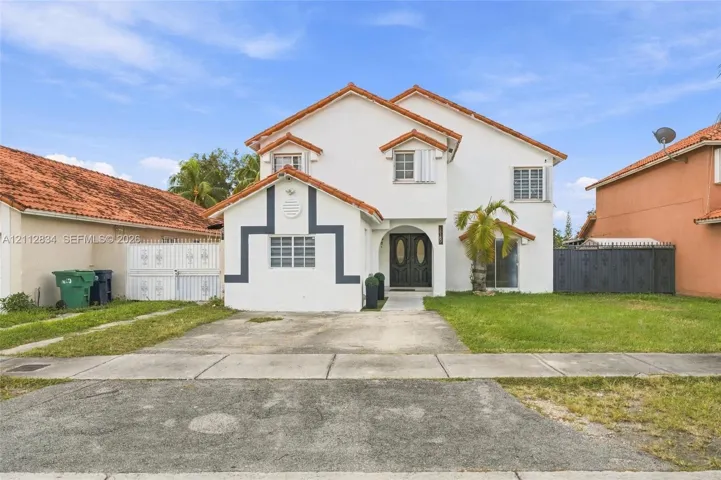 Two-story exterior featuring white stucco finish, a tile roof, decorative exterior trim, double-entry doors, and a concrete driveway
