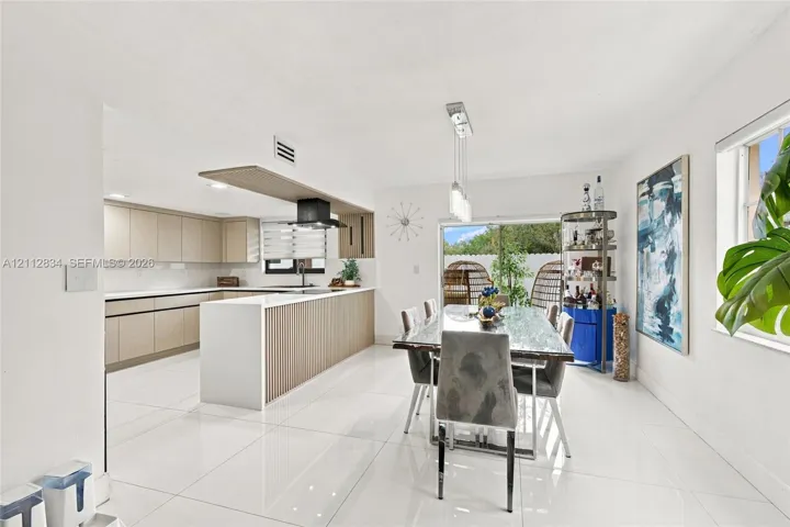 Kitchen featuring flat-panel cabinetry, a quartz waterfall island with fluted detailing, a matte black range hood, and large-format porcelain tile flooring