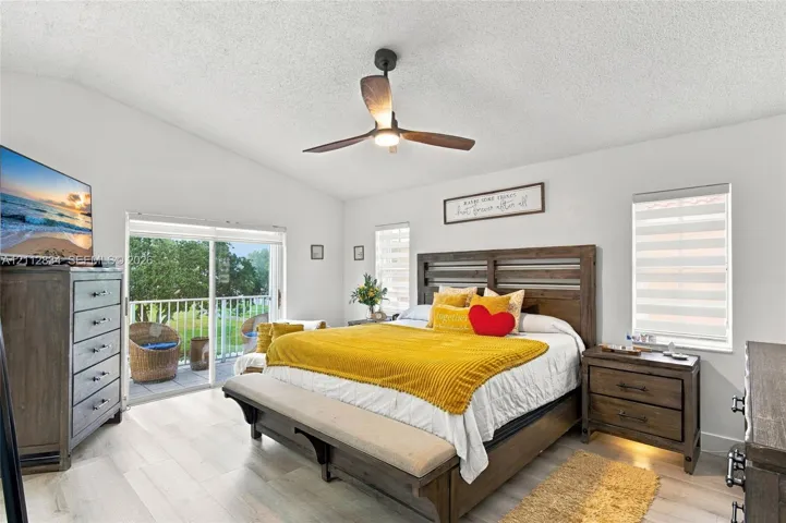 Vaulted ceilings, wood-finish flooring, ceiling fan with integrated lighting, and sliding glass doors providing outdoor access