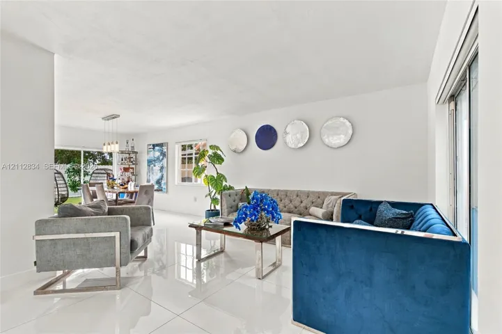Large-format neutral tile flooring, multi-pane window, and sliding glass door with access to exterior space, accented by a modern multi-pendant light fixture