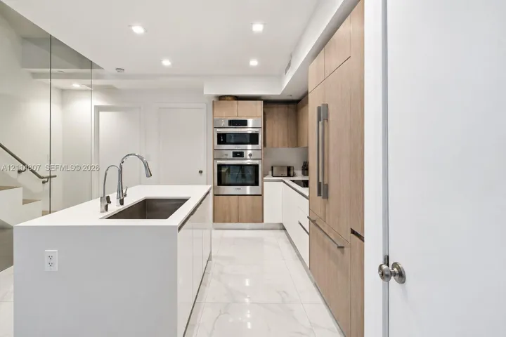 Kitchen featuring a center island with a solid surface countertop, stainless steel double wall ovens, wood-finish cabinetry, built-in panel-ready refrigerator, and stone-finish flooring