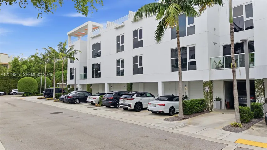 Contemporary multi-story exterior featuring a white smooth-stucco finish, recessed covered parking, multiple private balconies with glass railings, and a rooftop terrace