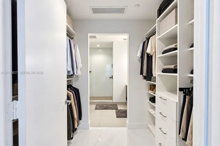 Walk-in closet featuring white built-in shelving, integrated dresser drawers, hanging rods, and large-format tile flooring