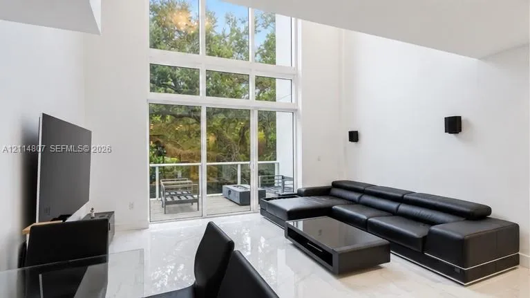 Double-height floor-to-ceiling windows, polished tile flooring, and exterior deck access