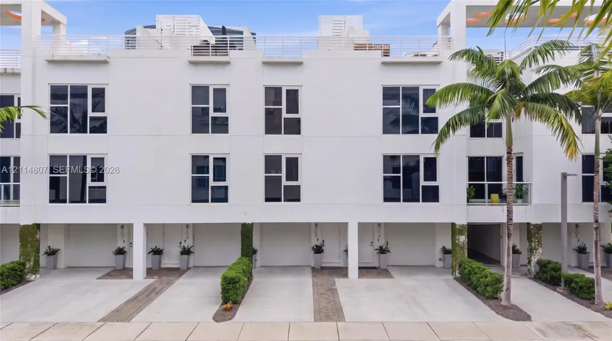 Modern multi-level exterior featuring white stucco facade, large multi-pane windows, ground-level garage access with individual concrete driveways, and upper-level rooftop terrace railings