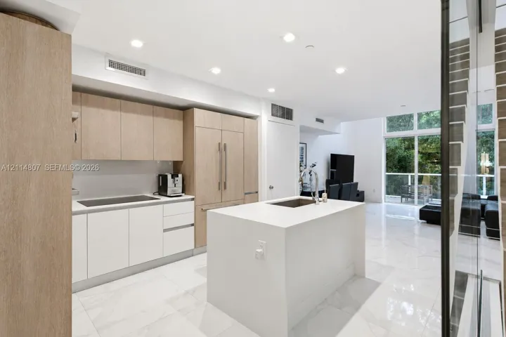 Kitchen featuring light wood-finish cabinetry, a white stone-surface island, built-in panel-ready refrigerator, and polished stone-finish flooring with floor-to-ceiling windows