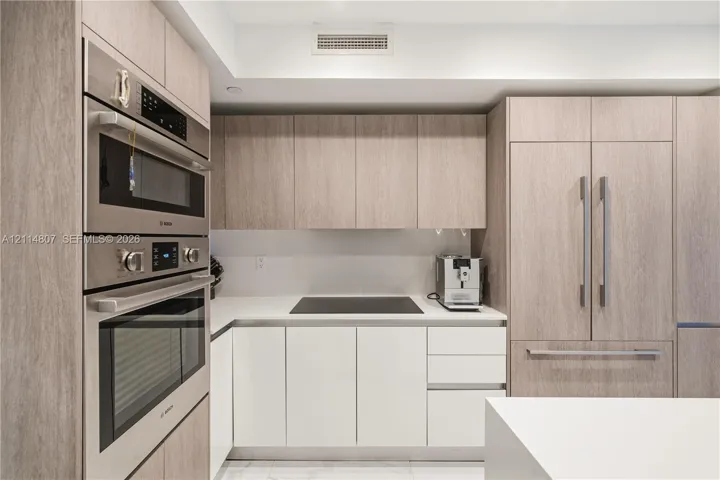 Custom wood-finish cabinetry, stainless steel built-in double wall ovens, integrated refrigerator, solid surface countertops, and smooth cooktop