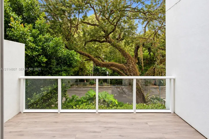 Covered balcony with wood-finish flooring, white railing, and glass panel inserts