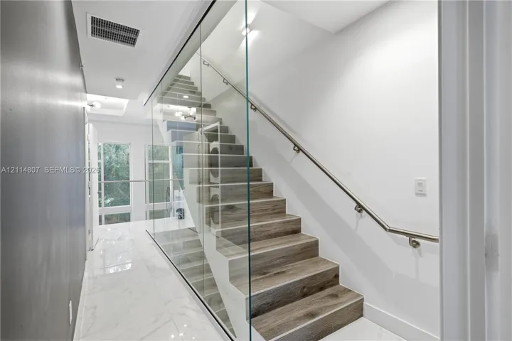 Staircase featuring wood-finish treads, a full-height glass partition, and a metal handrail, complemented by large-format porcelain tile flooring