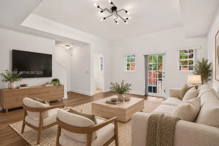 Living area featuring a tray ceiling, wood-finish flooring, multi-arm sputnik lighting fixture, and a glass-paneled exterior door