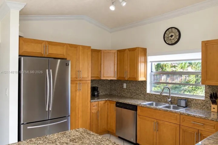 Kitchen featuring natural wood cabinetry, stone-surface countertops, a double-basin stainless steel sink with gooseneck faucet, stainless steel appliances, and crown molding