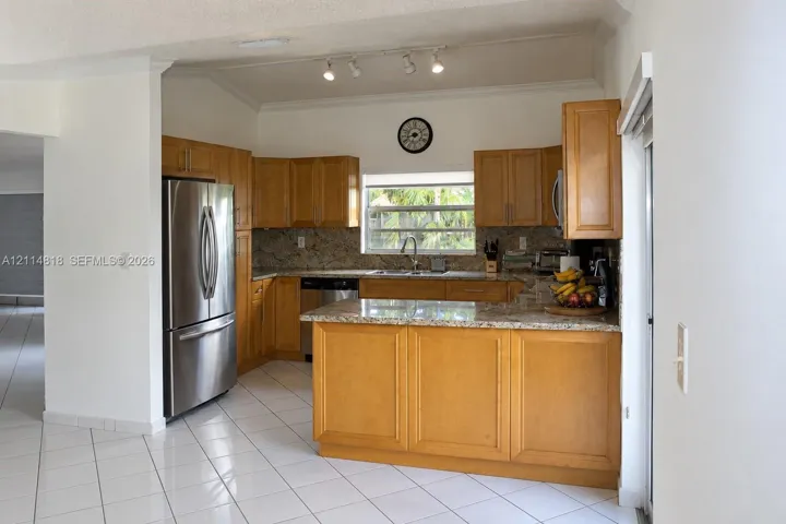 Kitchen featuring natural wood cabinetry, stone countertops, stainless steel appliances, tile flooring, and track lighting