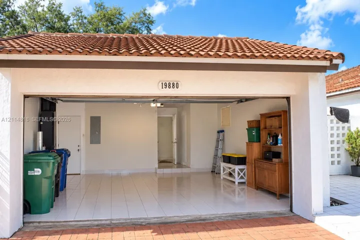 Attached two-car garage featuring a terracotta tile roof, white stucco exterior, and uniform ceramic tile flooring