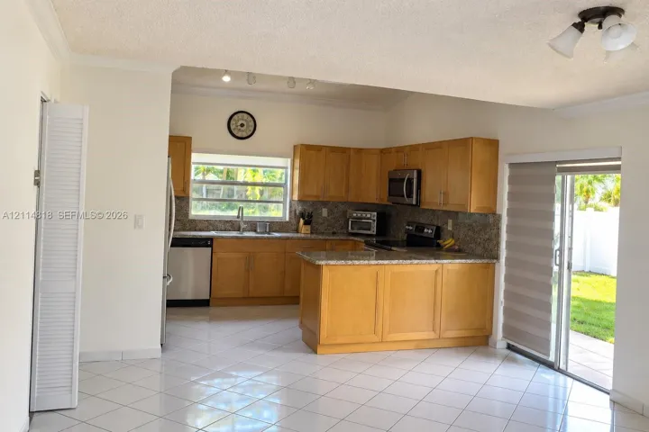 Kitchen featuring light wood cabinetry, stone countertops, stainless steel appliances, tile flooring, and sliding glass doors to the exterior