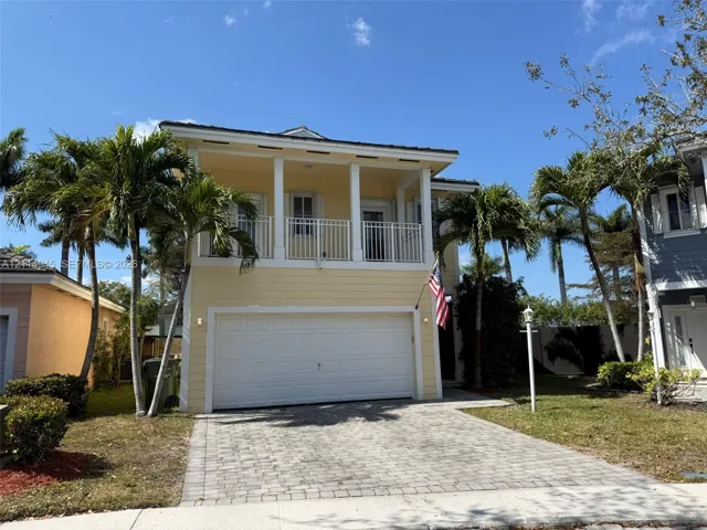 Two-story residence featuring a paved driveway, covered upper-level balcony with white railings, and attached two-car garage
