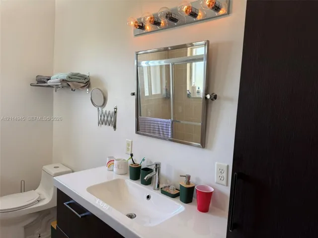 Vanity with integrated sink and countertop, pivoting chrome-framed mirror, five-bulb vanity light fixture, and wall-mounted towel shelf