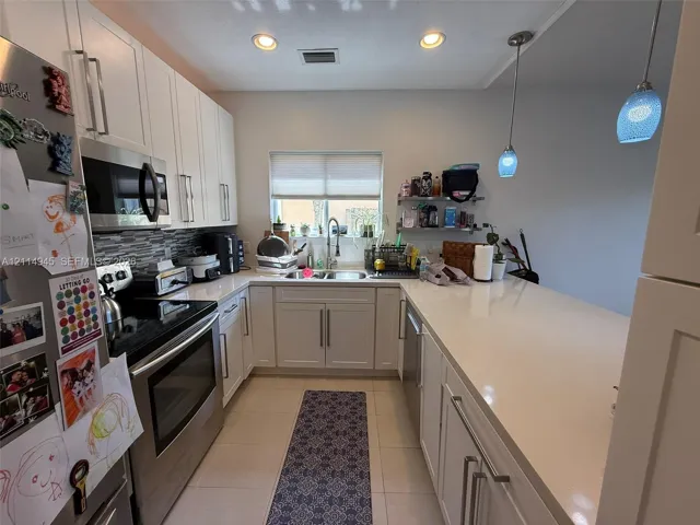 Kitchen featuring white shaker-style cabinetry, solid-surface countertops, stainless steel appliances, a multi-tonal linear tile backsplash, and dual glass pendant lighting