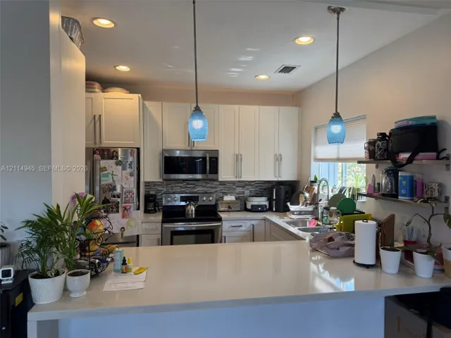 Kitchen featuring white shaker-style cabinetry, a quartz countertop island, stainless steel appliances, a multi-tone tile backsplash, and decorative pendant lighting