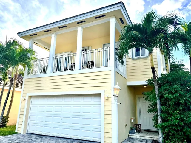 Two-story exterior with horizontal siding, a second-level railed balcony, an attached garage with a paneled door, and stone-paver driveway