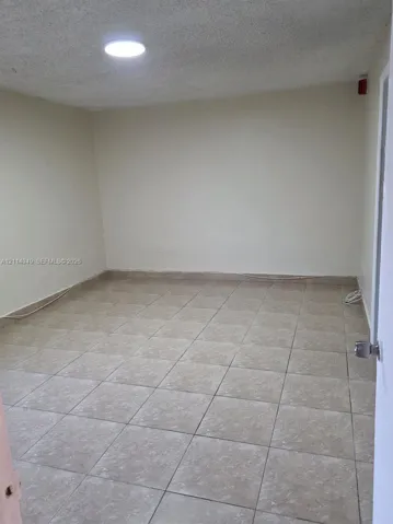 Interior room featuring neutral-toned tile flooring, textured ceiling, and a flush-mount circular lighting fixture
