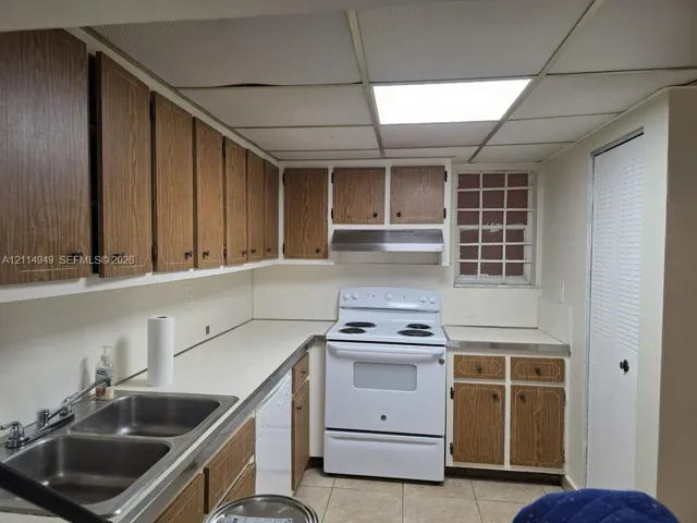 Kitchen featuring wood-finish cabinetry, white solid-surface countertops, dual-basin stainless steel sink, electric range, and a stainless steel range hood