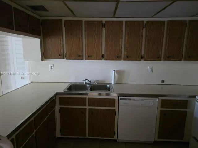 Kitchen featuring wood-finish cabinetry, white countertops, double-basin stainless steel sink, and a built-in dishwasher