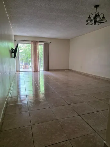 Large room featuring tile flooring, a multi-arm chandelier, and sliding glass doors with external iron railing