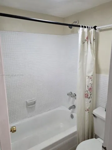 Bathroom featuring a white porcelain tub, square tile surround, built-in soap dish, and wall-mounted metal plumbing fixtures