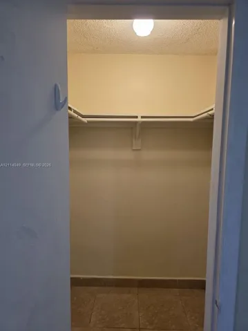 Closet featuring tile flooring, built-in shelving, a hanging rod, and overhead lighting
