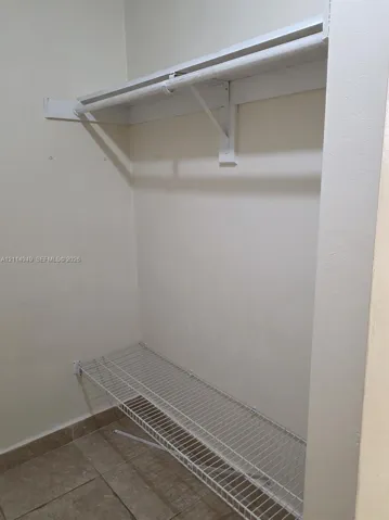 Storage space featuring neutral tile flooring, built-in white overhead shelving with a clothing rod, and a wire rack shelf