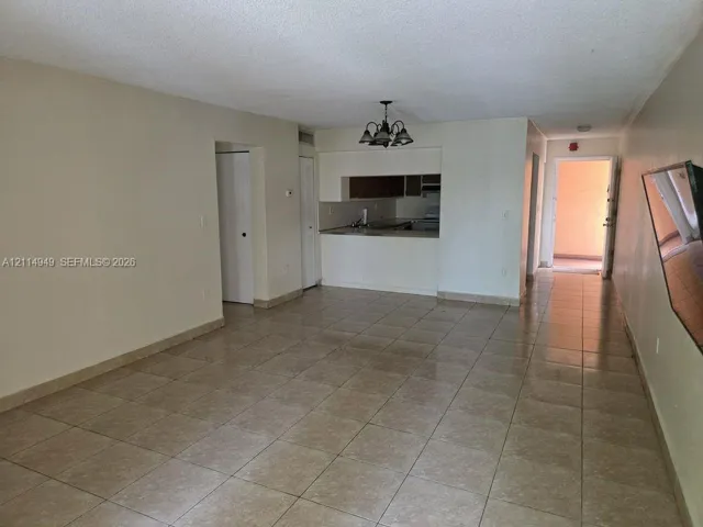 Open-concept interior featuring neutral wall tones, large-format tile flooring, a pass-through kitchen counter, and a multi-arm overhead light fixture