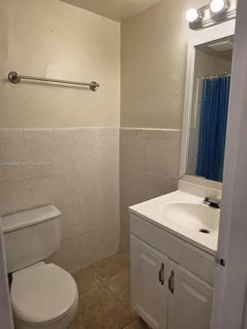 Bathroom featuring a white vanity cabinet with an integrated sink, ceramic tile wainscoting, tiled flooring, and a wall-mounted light fixture above the vanity mirror