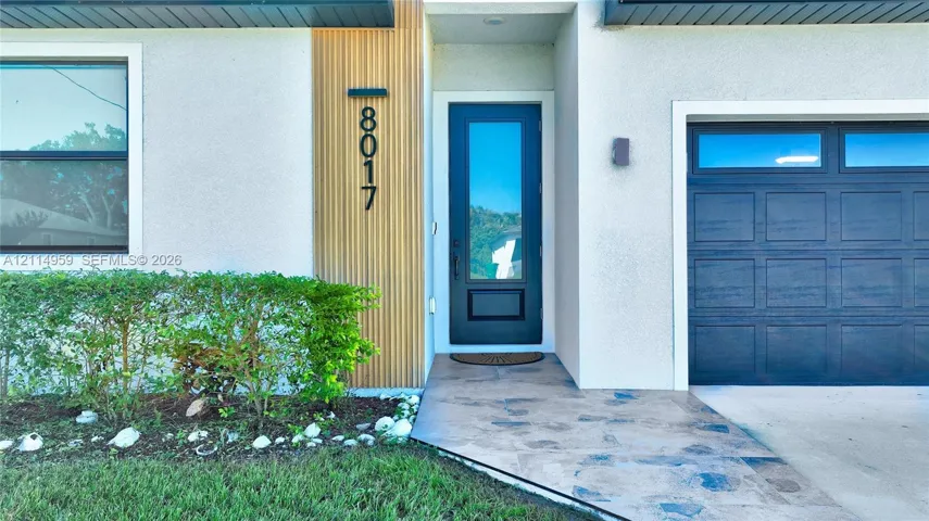 Modern entryway featuring a vertical wood-slat accent, black-framed glass panel door, stone-finish walkway, and multi-pane garage door