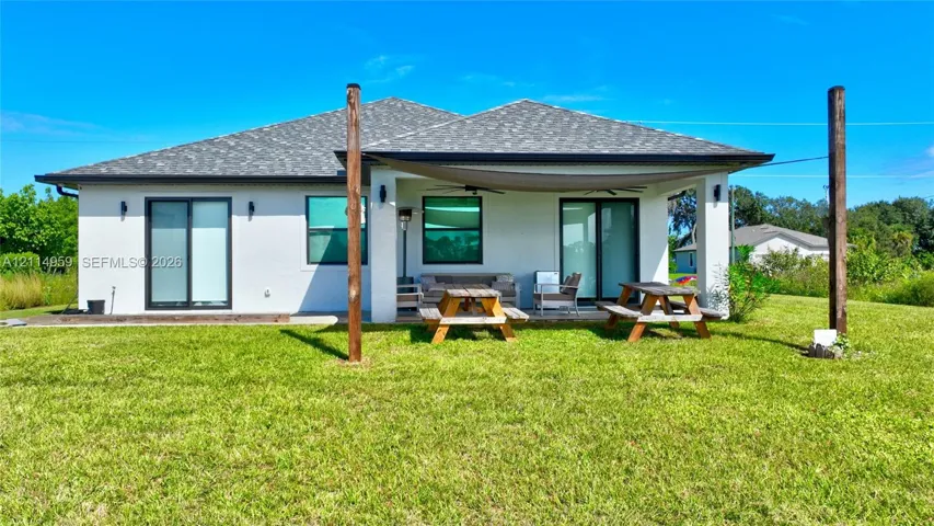 Rear exterior featuring a covered patio, dual sliding glass door entries, shingle roof, and expansive lawn