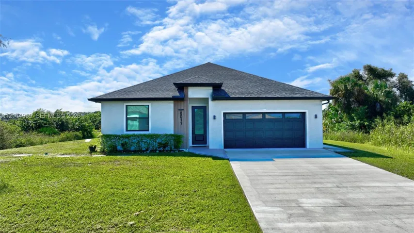 Single-story exterior featuring a light-toned stucco façade, wood-finish entryway accent, attached two-car garage, and a hip roofline