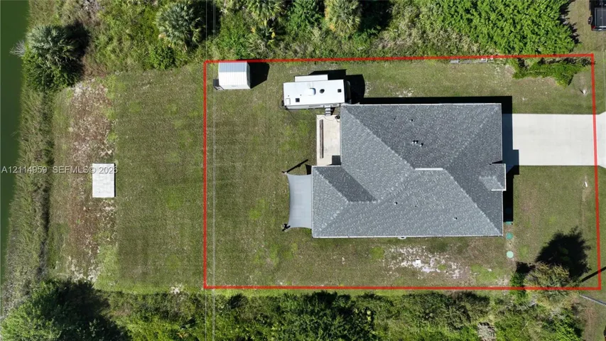 Aerial perspective of the property featuring a concrete driveway, multi-faceted roof structure, detached metal storage building, and grass-covered lot