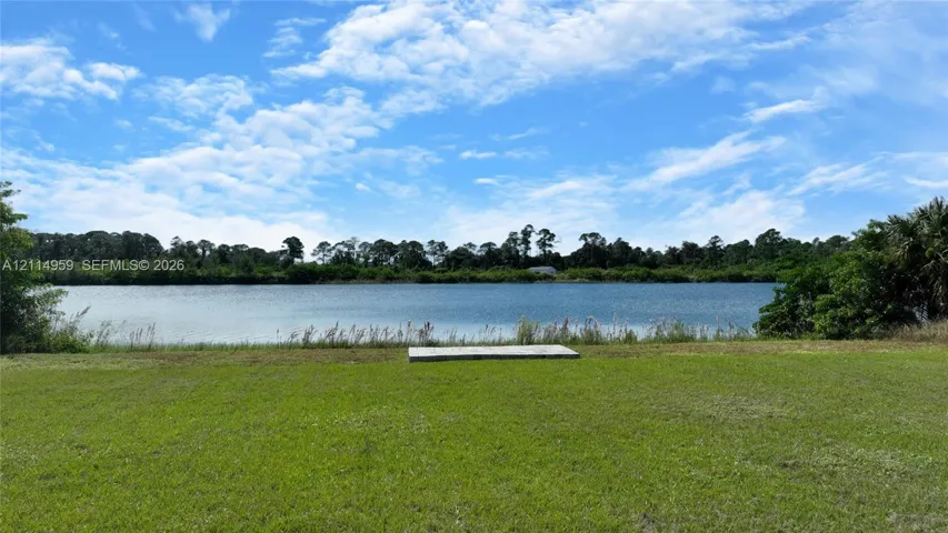 Waterfront lot featuring a manicured lawn, a concrete pad, and mature perimeter trees