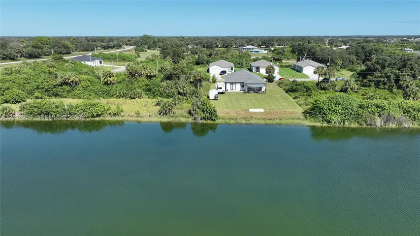 Waterfront property featuring a landscaped lawn, paved driveway, and shingle-roof structure