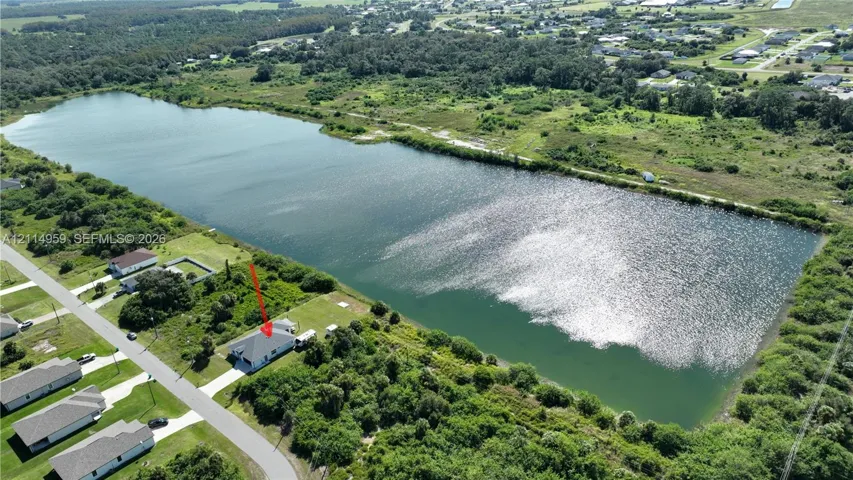 Aerial perspective of a property featuring a single-family residence, concrete driveway, and direct water frontage on a large lake