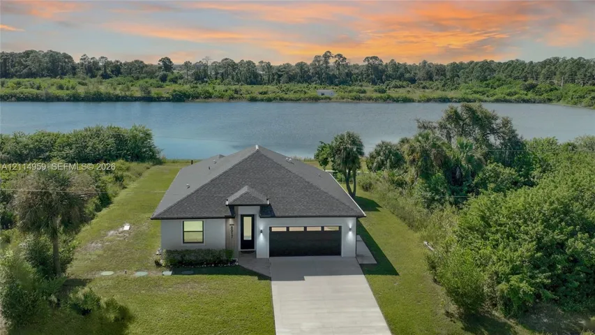 Single-story residence featuring a dark shingled roof, stucco exterior, concrete driveway, attached multi-car garage, and waterfront positioning