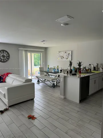 Open-concept living space featuring wood-finish tile flooring, kitchen island with stone countertop, and sliding glass doors to the exterior