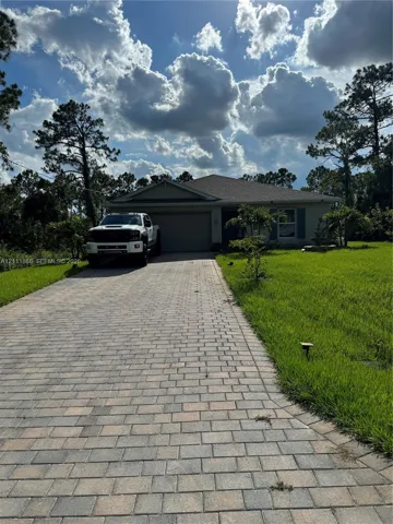 Single-story residence featuring a paved brick driveway, attached garage, and mature trees on the lot